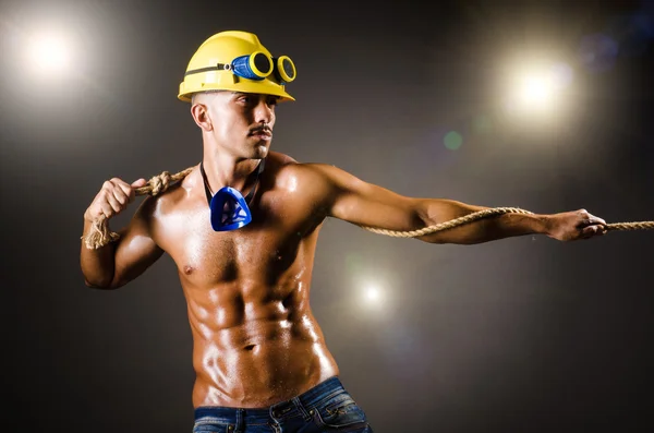 Constructor desnudo tirando de la cuerda en la oscuridad — Foto de Stock