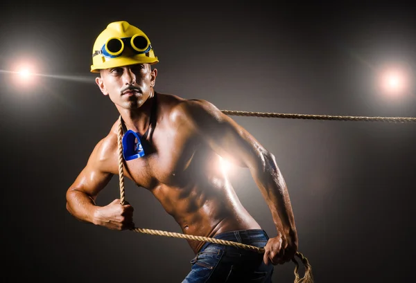 Nude builder pulling rope in darkness — Stock Photo, Image