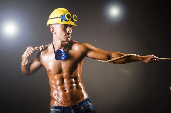 Constructor desnudo tirando de la cuerda en la oscuridad — Foto de Stock