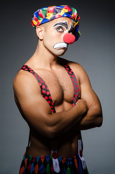 Sad clown against dark background, arms crossed