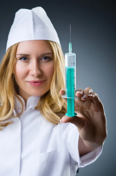 Woman doctor with syringe in dark studio — Stock Photo, Image