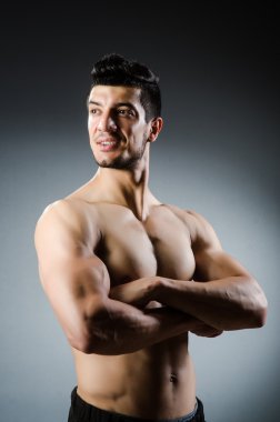 Kaslı adam karanlık stüdyoda poz veriyor.