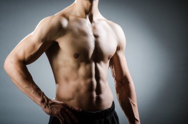 Kaslı adam karanlık stüdyoda poz veriyor.