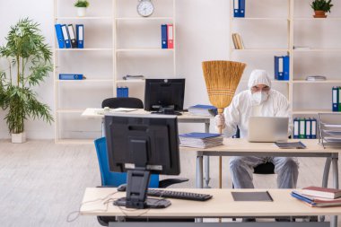 Yaşlı müteahhit elinde süpürgeyle ofisi temizliyor.