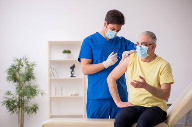 Yaşlı erkek hasta aşılama bölümünde genç bir erkek doktor.
