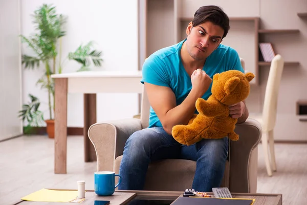 Genç adam evde ayı oyuncağıyla oturuyor. — Stok fotoğraf