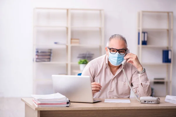 Velho empregado do sexo masculino que trabalha no local de trabalho durante a pandemia — Fotografia de Stock