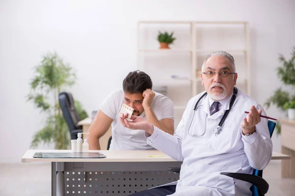 Vecchio medico maschile suggerendo pillole per il giovane paziente maschio — Foto Stock