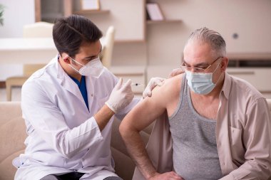 Genç erkek doktor aşı konseptinde yaşlı hastayı ziyaret ediyor.
