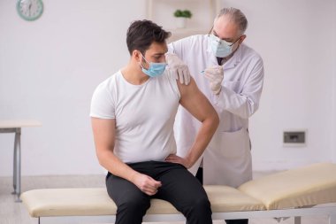 Genç erkek hasta yaşlı erkek doktoru aşıyla ziyaret ediyor.