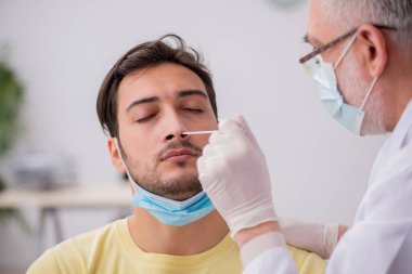 Genç erkek hasta yaşlı doktor otorhinolaryngologis 'i ziyaret ediyor.