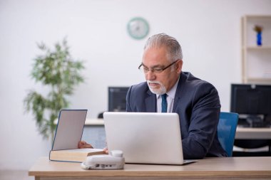 Ofiste kitap okuyan yaşlı bir erkek.