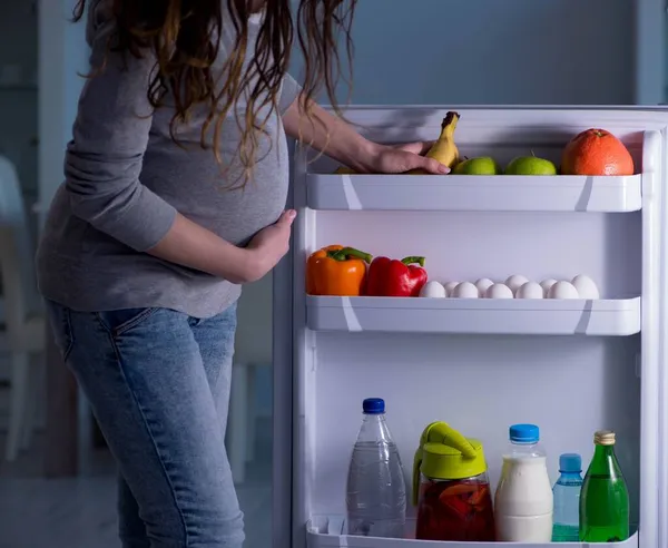 Mulher grávida perto de geladeira à procura de alimentos e lanches à noite — Fotografia de Stock