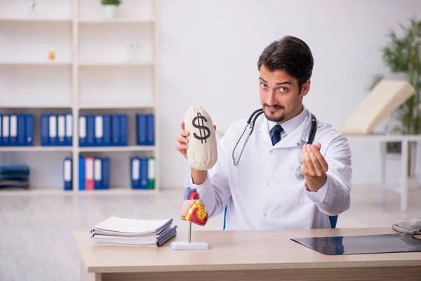 Молодой врач-кардиолог держит мешок с деньгами — стоковое фото