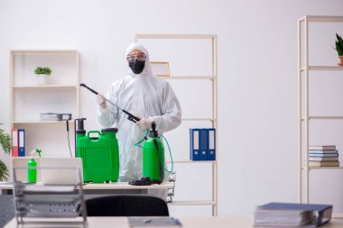 Young male contractor disinfecting office during pandemic
