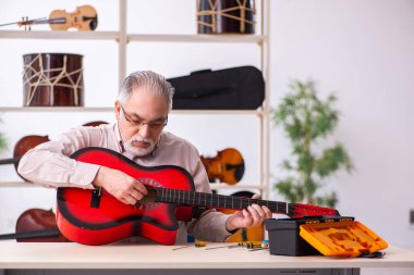 Yaşlı erkek tamirci iş yerinde müzik aletlerini tamir ediyor.