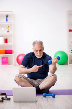 Yaşlı adam içeride spor egzersizleri yapıyor.