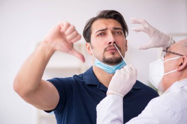 Genç erkek hasta salgın sırasında yaşlı erkek doktoru ziyaret ediyor.