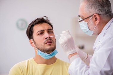 Genç erkek hasta yaşlı doktor otorhinolaryngologis 'i ziyaret ediyor.