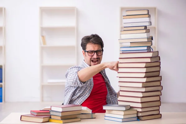 Fiatal férfi diák és túl sok könyv az osztályteremben. — Stock Fotó