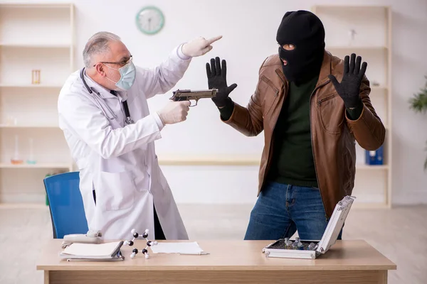 Человек в маске грабитель крадет вакцину у старого доктора — стоковое фото