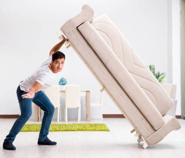 Genç adam evde mobilya taşıyor.