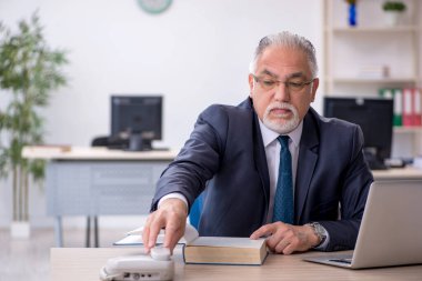 İş yerinde yaşlı bir erkek çalışan telefonda konuşuyor.