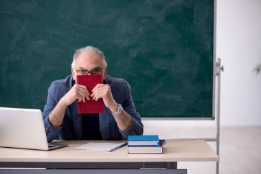 Sınıfta kitap tutan yaşlı bir erkek öğretmen.