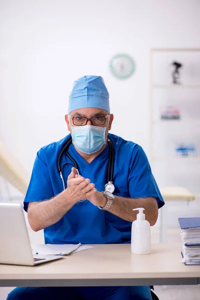 Yaşlı erkek doktor salgın sırasında klinikte çalışıyor. — Stok fotoğraf