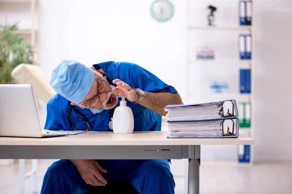 Oude mannelijke arts werkzaam in de kliniek tijdens pandemie — Stockfoto