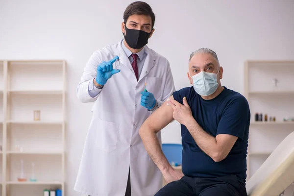 Alte männliche Patientin besucht jungen männlichen Arzt im Impfpass — Stockfoto