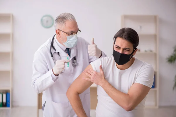 Junge männliche Patienten besuchen alten Arzt im Impfkonzept — Stockfoto