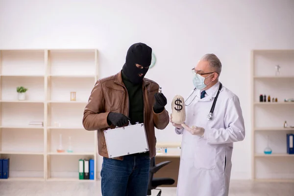Hombre enmascarado ladrón sobornando a viejo doctor para conseguir la vacuna —  Fotos de Stock