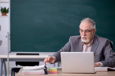 Tahtanın önünde yaşlı bir erkek öğretmen.