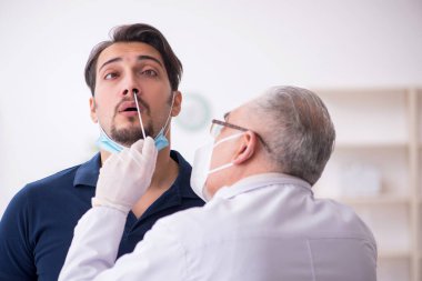 Genç erkek hasta salgın sırasında yaşlı erkek doktoru ziyaret ediyor.