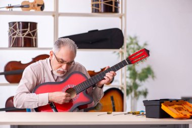 Yaşlı erkek tamirci iş yerinde müzik aletlerini tamir ediyor.