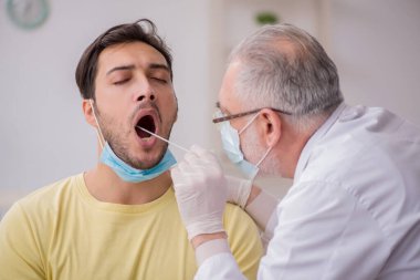 Genç erkek hasta yaşlı doktor otorhinolaryngologis 'i ziyaret ediyor.