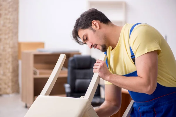 Jovem carpinteiro masculino reparando cadeira no escritório — Fotografia de Stock