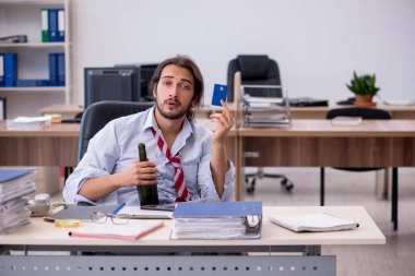 Genç erkek çalışan ofiste alkol içiyor.