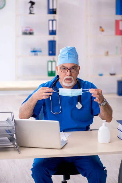 Old male doctor working in the clinic during pandemic — Stock Photo, Image