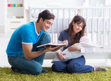 Yeni doğmuş bebekleriyle halıda oturan genç ebeveynler.