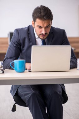 Genç erkek çalışan işyerinde oturuyor.