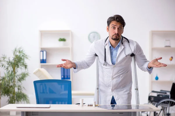 Jonge mannelijke arts met krukken in de kliniek — Stockfoto