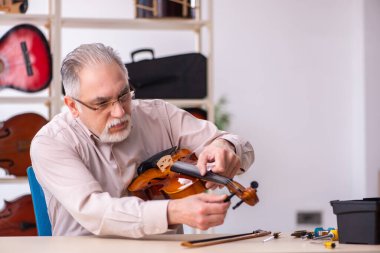 Yaşlı erkek tamirci iş yerinde müzik aletlerini tamir ediyor.