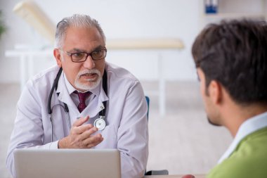 Genç erkek hasta yaşlı erkek doktoru ziyaret ediyor.