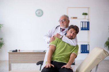 Genç erkek hasta yaşlı erkek doktoru ziyaret ediyor.