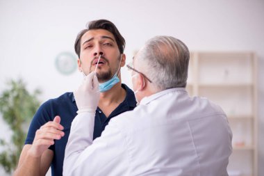 Genç erkek hasta salgın sırasında yaşlı erkek doktoru ziyaret ediyor.