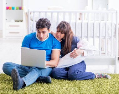 Yeni doğmuş bebekleriyle halıda oturan genç ebeveynler.