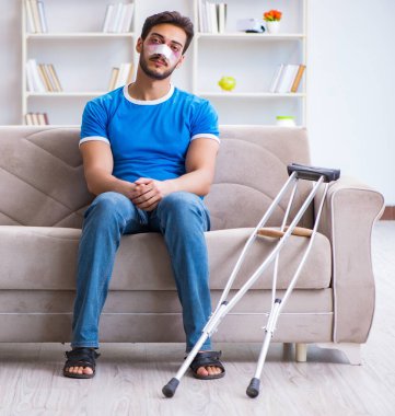 Koltuk değnekli yaralı bir adam evde iyileşiyor.