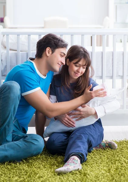 Yeni doğmuş bebekleriyle halıda oturan genç ebeveynler.